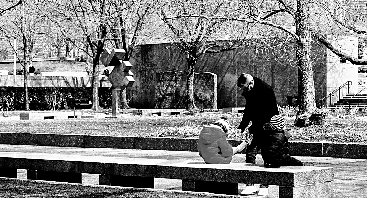 Black and white photo of a parent tying children's shoes in a park.